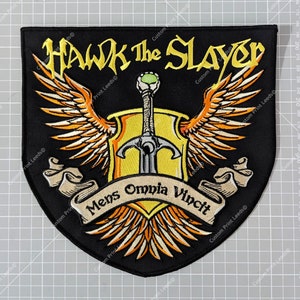 May include: Black embroidered patch with a yellow and orange winged shield, a sword, and the text "HAWK The SLAYER" in yellow. The text "Mens Omnia Vincit" is on a white scroll.