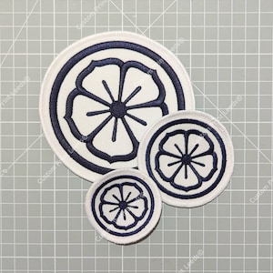 May include: Three circular embroidered patches in white and navy blue. Each patch features a floral design with a central circle and radiating lines. The patches are of different sizes and have a navy blue border.