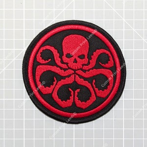 Op de afbeelding: Rode en zwarte geborduurde patch met een schedel en tentakels, vergelijkbaar met het logo van de fictieve organisatie HYDRA.