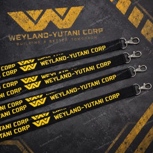 May include: Four black lanyards featuring the yellow Weyland-Yutani Corp logo and text. Each strap includes a silver-toned metal swivel lobster clasp at the end. The design repeats the company name and stylised W logo in a bold yellow font against the black fabric.