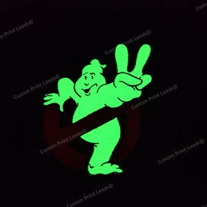 May include: A green glow-in-the-dark ghost with a peace sign hand gesture. The ghost is in front of a red circle with a diagonal line through it. The background is black.