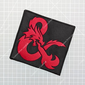 May include: A red and black embroidered patch featuring a stylised dragon with a D&D symbol. The patch is square and has a black background with a red dragon.