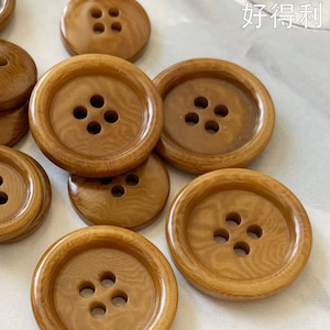 May include: A collection of 13 brown wooden buttons with four holes each. The buttons are arranged in a random pattern on a white surface. The text "Hodeli 好得利" and "www.hodelihk.com" are visible in the image.