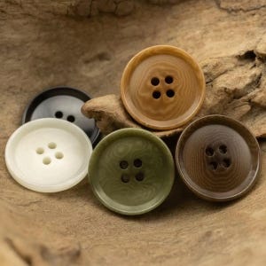 Peut inclure: Cinq boutons de différentes couleurs, chacun avec quatre trous. Les boutons sont faits d'un matériau texturé et ont une apparence de bois. Les couleurs sont le noir, le blanc, le brun, le vert et le beige.