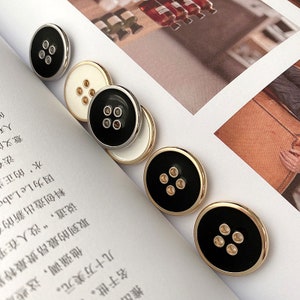 May include: Five round buttons with a black center and gold or silver trim. The buttons have five gold circles in the center.