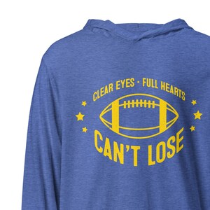 Puede incluir: Una sudadera con capucha de manga larga azul real con un gráfico de fútbol amarillo y el texto "CLEAR EYES - FULL HEARTS CAN'T LOSE" impreso en la parte delantera.