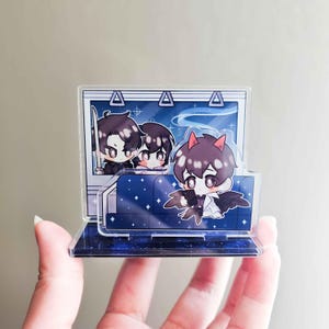 Könnte beinhalten: Ein klarer Acrylständer mit Anime-Charakteren. Das Design umfasst einen Zuginnenraum mit drei Figuren, eine davon mit Teufelshörnern und Flügeln. Der Sockel und der Hintergrund haben ein Sternennacht-Thema mit blauen und weißen Akzenten.