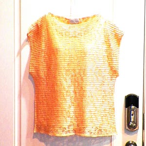 May include: A sleeveless, orange and white, knit top with a scoop neck. The top has a woven texture and a label that reads "Icon" in the center of the neckline.