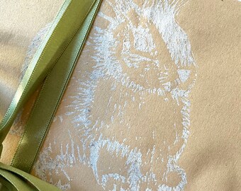 Könnte beinhalten: Eine braune Papiertüte mit einem weißen Hasenmotiv und einem grünen Satinband.