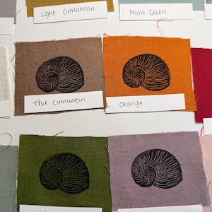 May include: Fabric swatches in a range of colours, each with a black seashell print. Colours include true cinnamon, orange, and red. Each swatch is labelled with its colour name.