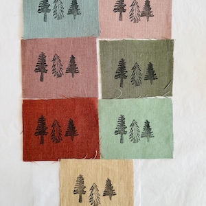 May include: Eight fabric squares with a black silhouette of three pine trees printed on each. The squares are in various colours: light blue, pink, red, green, beige, and two shades of brown.
