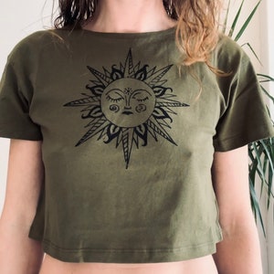 Può includere: Top corto verde oliva con grafica di un sole nero. Il sole ha gli occhi chiusi e linee radianti. La maglietta a maniche corte è realizzata in materiale morbido. Il disegno del sole è centrato sul davanti.