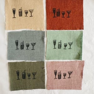 Op de afbeelding: Vijf stofstalen met een zwart inktontwerp van vier verschillende soorten glazen met een rietje. De stalen zijn in de kleuren beige, rood, blauw, groen en roze.