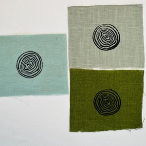 May include: Three fabric squares with a black and white concentric circle design printed on each. The squares are light blue, light green, and dark green.