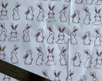 Könnte beinhalten: Weißes Papier mit einem sich wiederholenden Muster aus braunen Hasenillustrationen. Die Hasen sind in verschiedenen Posen dargestellt, mit langen Ohren und einfachen Gesichtszügen. Ein Edelstahl-Lineal liegt diagonal, mit Zoll-Messungen.