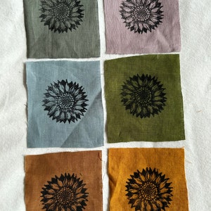 Puede incluir: Seis cuadrados de tela con una impresión de girasol negro en cada uno. Los cuadrados son de diferentes colores: verde, morado, azul, verde oliva, marrón y amarillo.