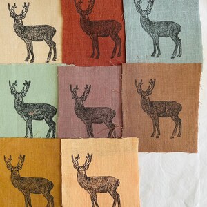 May include: Nine fabric squares with a black silhouette of a deer printed on each. The squares are in various colours, including beige, brown, red, green, and pink.