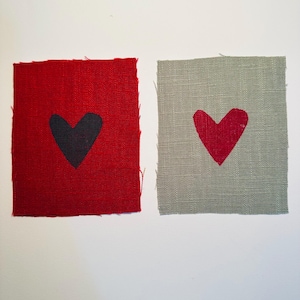 Könnte beinhalten: Zwei Stoffquadrate mit einem Herzmotiv. Das Quadrat links ist rot mit einem schwarzen Herzen. Das Quadrat rechts ist grau mit einem roten Herzen.