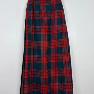 Peut inclure: Longue jupe plissée à motif écossais classique. La jupe présente une combinaison de couleurs rouge et vert foncé audacieuse, avec un motif quadrillé répétitif. La jupe est suspendue à un cintre, mettant en valeur toute sa longueur et son design.