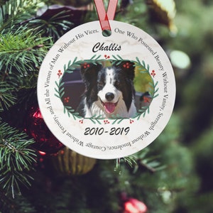 Op de afbeelding: Een witte ronde kerstbal met een foto van een zwart-witte border collie, een groene krans met rode bessen en de tekst "Challis 2010-2019". De kerstbal heeft een marmerachtige achtergrond met de tekst "One Who Possessed Beauty Without Vanity, Strength Without Insolence, Courage Without Ferosity, and All the Virtues of Man Without His Vices."