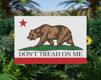 May include: A rectangular yard sign featuring the California state flag design. The sign displays a brown bear, a red star, and the text "DON'T TREAD ON ME" on a white background with a red stripe at the bottom. The sign is mounted on a metal stake.
