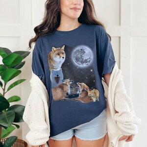 May include: A navy blue t-shirt with a graphic of foxes howling at the moon. The foxes are in a variety of colors, including white, brown, and orange. The moon is a full moon and is white with a gray center.