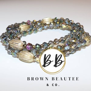 May include: A multi-strand bracelet with iridescent glass beads and gold accents. The bracelet is wrapped around a white background with the text "BB BROWN BEAUTEE & CO."