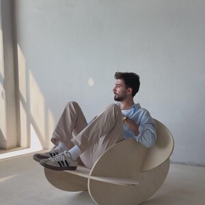 May include: A unique, modern rocking chair made of light-colored wood. The chair features a circular design with a curved seat and backrest. The chair is designed for comfort and style, perfect for a living room or bedroom.