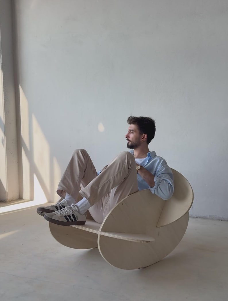 May include: A unique, modern rocking chair made of light-colored wood. The chair features a circular design with a curved seat and backrest. The chair is designed for comfort and style, perfect for a living room or bedroom.