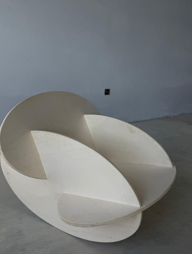 May include: A modern, abstract wooden sculpture with a light, natural finish. The piece features curved, intersecting planes, creating an open, three-dimensional form. The sculpture is designed to be a decorative art piece.