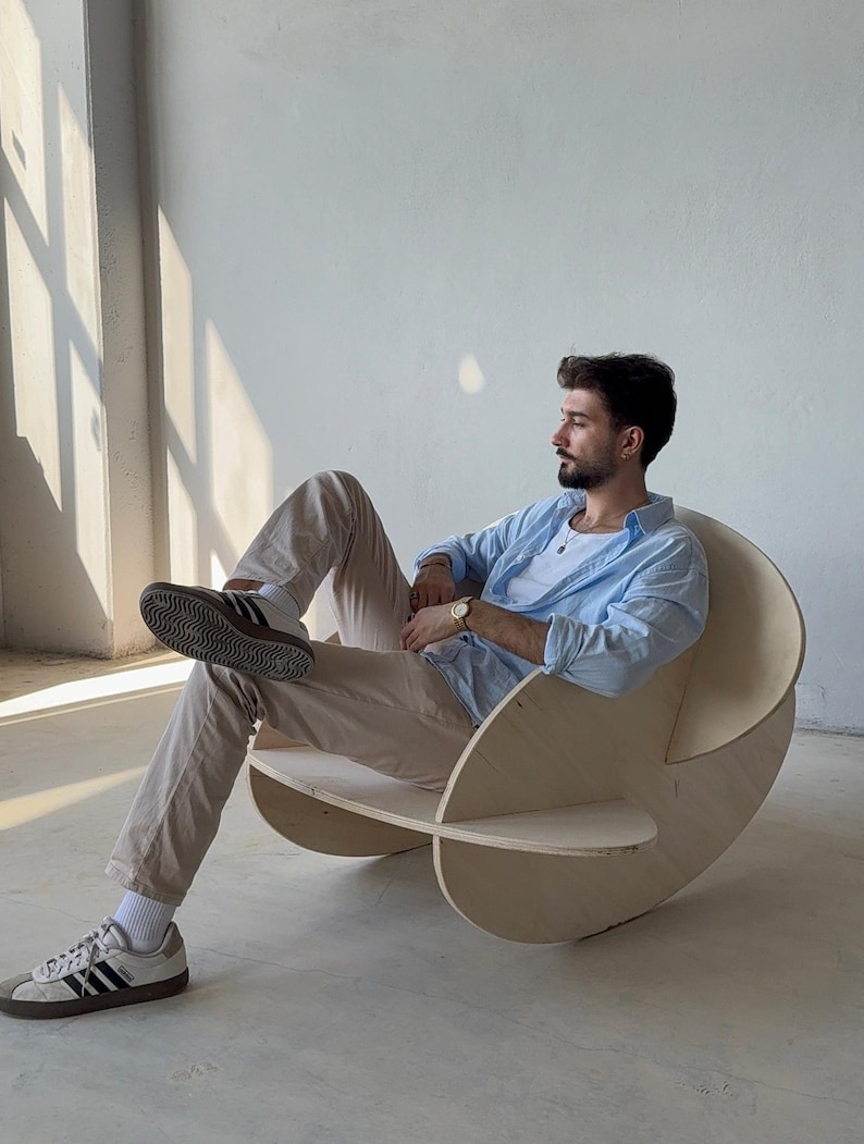 May include: A unique, modern wooden rocking chair with a light-colored finish. The chair features a distinctive design with curved, circular elements and a comfortable seat. The chair is designed for relaxation and adds a touch of contemporary style to any living space.