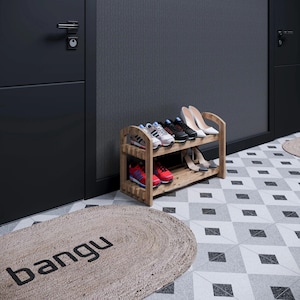 May include: A wooden shoe rack with two shelves, holding various pairs of shoes, including sneakers and heels. The rack is positioned in a hallway with a patterned floor and a rug with the word "bangu" on it.