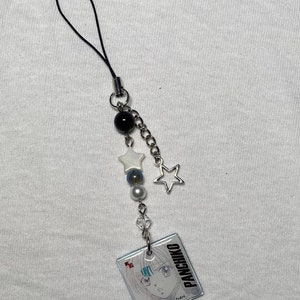 K&ouml;nnte beinhalten: Ein schwarz-wei&szlig;er Handy-Anh&auml;nger mit einer silbernen Kette und Stern-Anh&auml;ngern. Der Anh&auml;nger zeigt einen Comic-Charakter mit dem Text "PANCHIKO D>E>A>T>H>ME>T-AL".