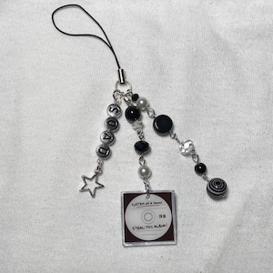 May include: A black and white phone charm with a silver star, black and white beads, and a small plastic CD with the text "System of a Down" and "Steal This Album!"