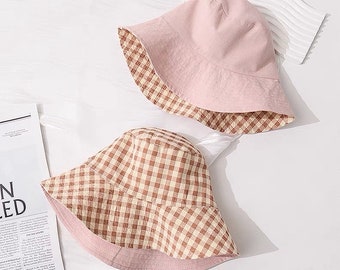 Puede incluir: Dos sombreros de cubo reversibles. Un lado es rosa y el otro lado es de cuadros marrones y blancos.