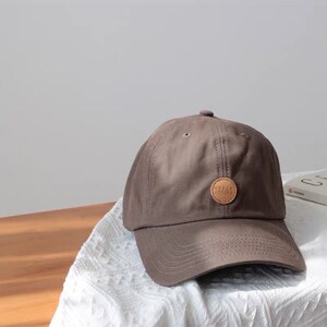 May include: A brown baseball cap with a brown leather patch that says "URBAN OUTFITTERS" in white lettering.