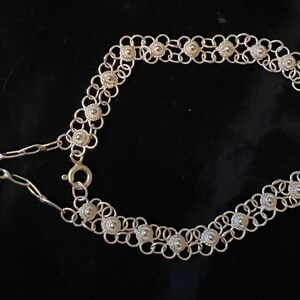 May include: A silver chain belt with a delicate design featuring small, round, textured beads. The belt has a clasp closure and a long, thin chain extension.