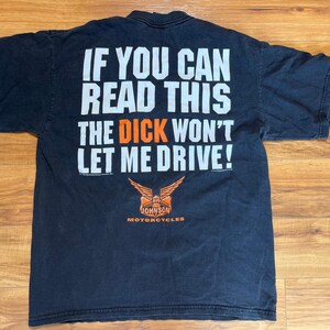 Puede incluir: Camiseta negra con texto blanco que dice "IF YOU CAN READ THIS THE DICK WON'T LET ME DRIVE!" en negrita. Debajo, un logotipo naranja y blanco de "Big Johnson Motorcycles".