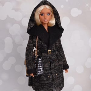 May include: A doll wearing a hooded black and gray coat with a black fur collar, a black belt, and a houndstooth purse. The doll is also wearing gray and white plaid pants and black and white heels.