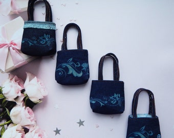 May include: Four small blue denim bags with floral designs. The bags have brown straps and are lined up in a row on a white surface.