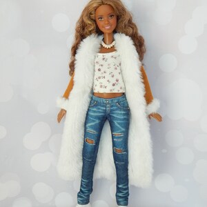 May include: A brown-haired doll wearing a white faux fur coat, a white and floral print top, blue jeans with distressed details, and white sneakers.