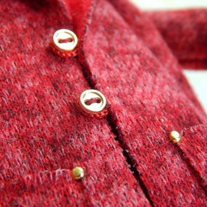 K&ouml;nnte beinhalten: Ein roter Strickcardigan mit goldenen Kn&ouml;pfen und einer Tasche auf der Vorderseite.