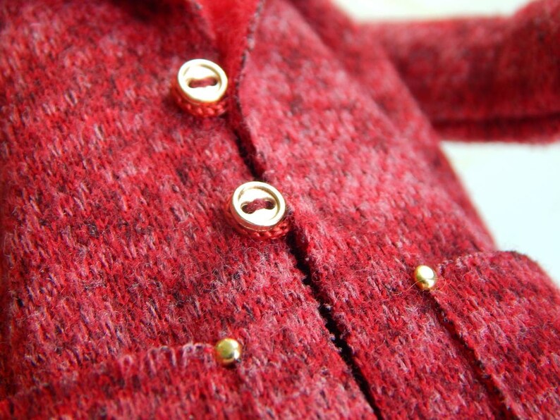 K&ouml;nnte beinhalten: Ein roter Strickcardigan mit goldenen Kn&ouml;pfen und einer Tasche auf der Vorderseite.