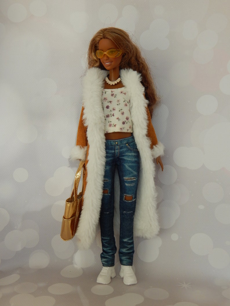 May include: A brown corduroy coat with a white faux fur lining, worn over a white floral top and blue jeans. The doll is wearing yellow sunglasses and a gold necklace.