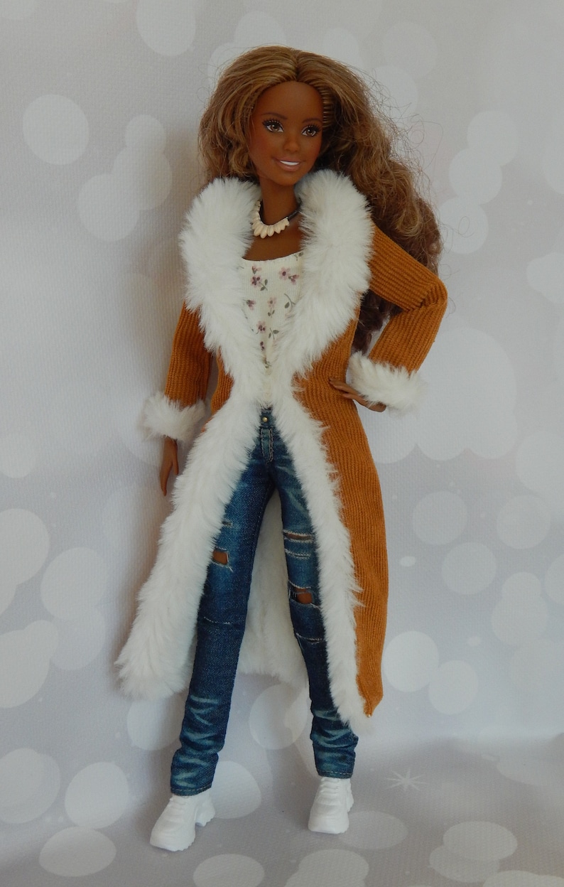 May include: A brown corduroy coat with a white faux fur trim. The coat is open and the doll is wearing blue jeans with rips and white sneakers.