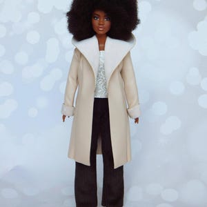 May include: A doll with brown skin and an afro hairstyle is wearing a beige coat with a white fur collar and cuffs, brown corduroy pants, and white shoes.