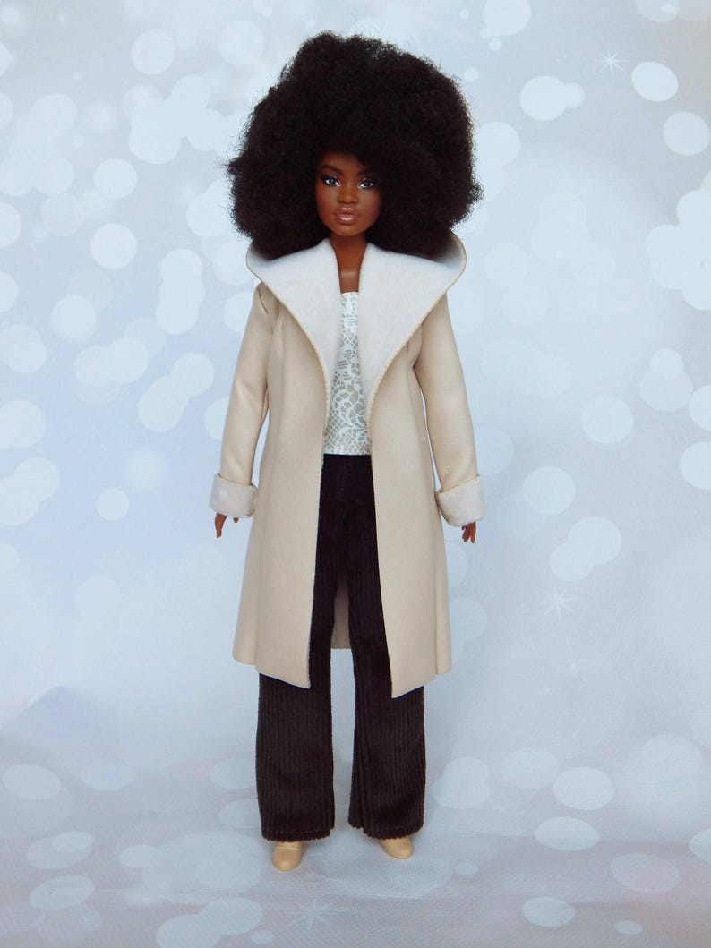 May include: A doll with brown skin and an afro hairstyle is wearing a beige coat with a white fur collar and cuffs, brown corduroy pants, and white shoes.