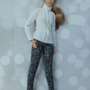 May include: A white cable knit turtleneck sweater with a black and white patterned pair of pants. The doll is wearing black shoes.