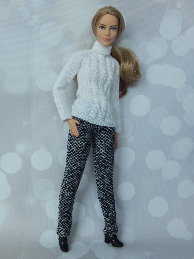May include: A white cable knit turtleneck sweater with a black and white patterned pair of pants. The doll is wearing black shoes.