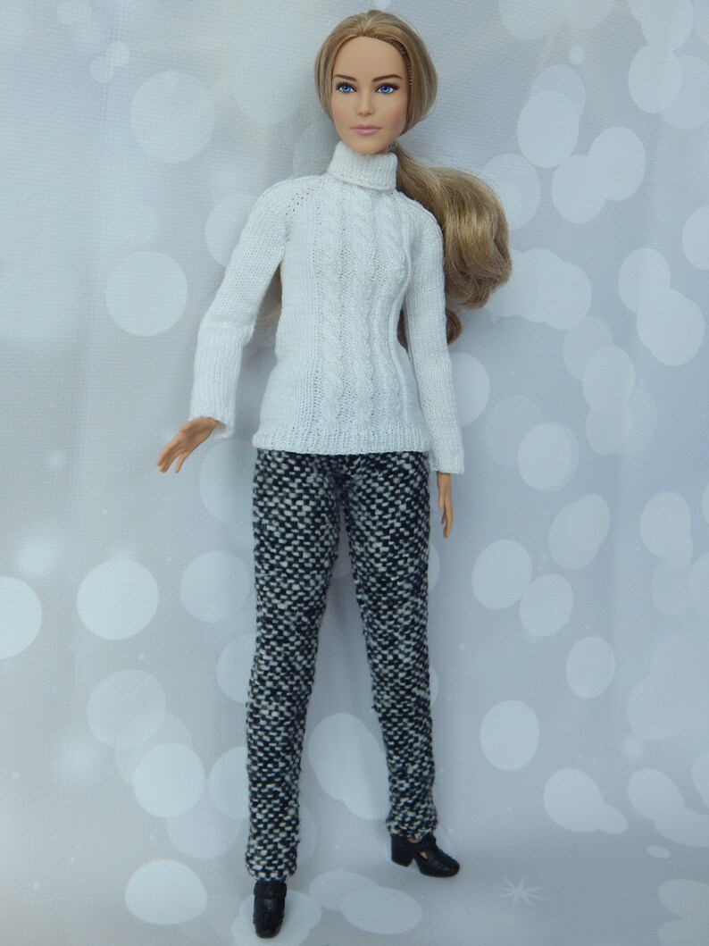May include: A doll wearing a white turtleneck sweater and black and white patterned pants. The doll has long blonde hair and blue eyes.